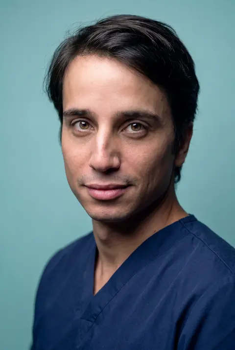 AI example headshot: man in navy scrubs on a light blue background