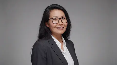 AI example headshot: woman with glasses in a dark blazer on a gray background