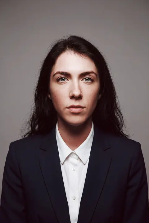 AI example headshot: woman with long dark hair in a navy blazer and white shirt
