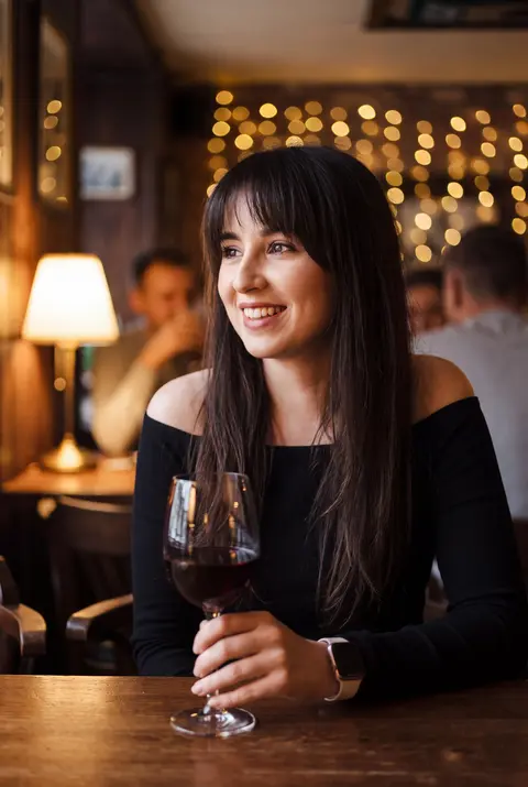AI example dating photo: young woman holding a glass of red wine in a cozy pub