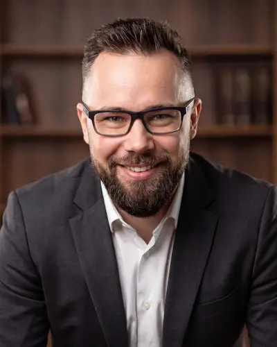 AI example made from that photo: the same man in a dark blazer in front of bookshelves