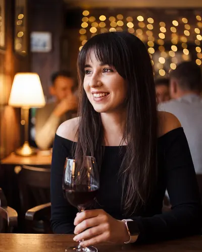 AI example made from that photo: the same woman in a black top with a glass of red wine in a warm bar